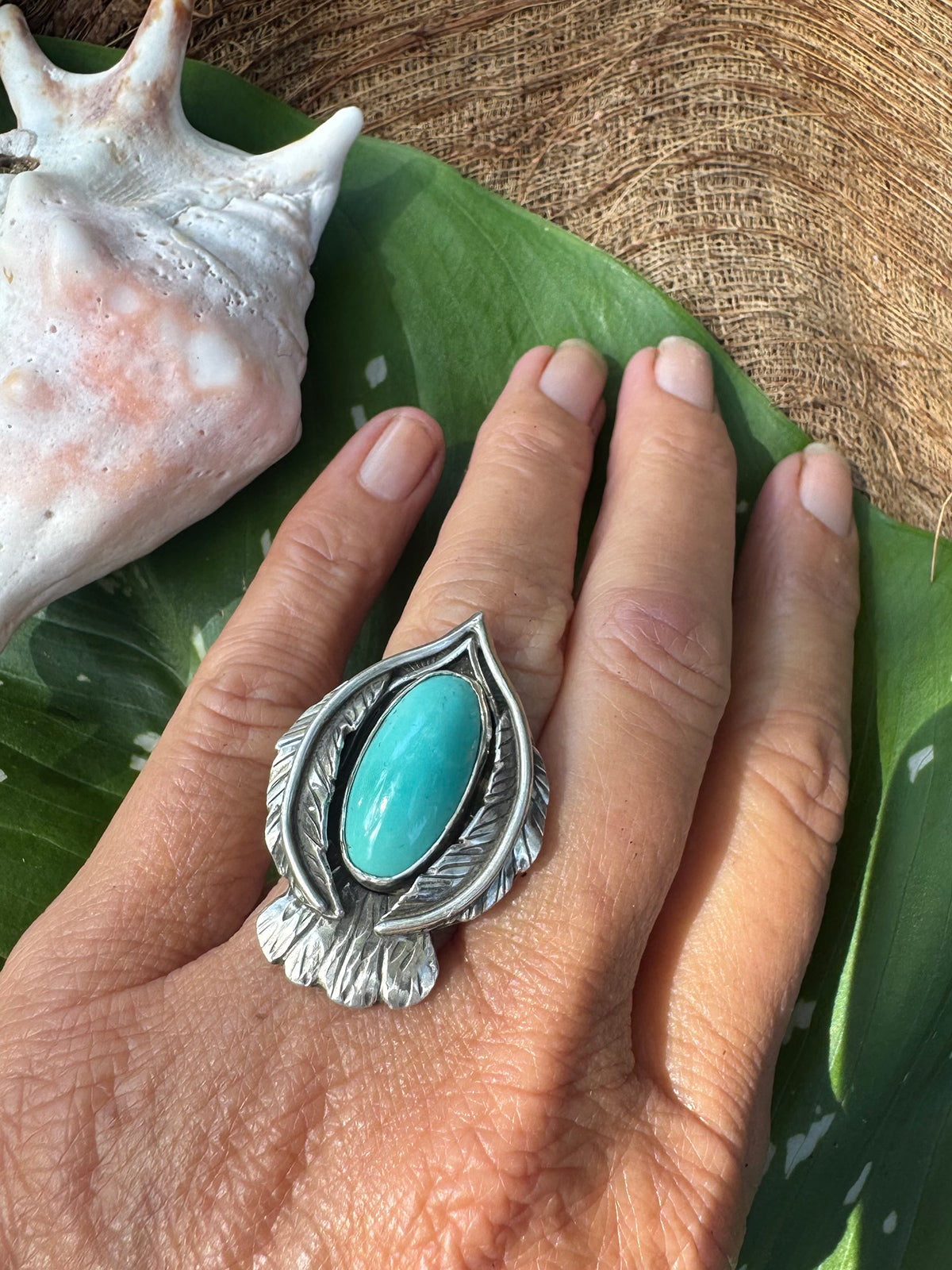 Hand wearing a bird shape silver ring with a turquoise stone on a leafy background