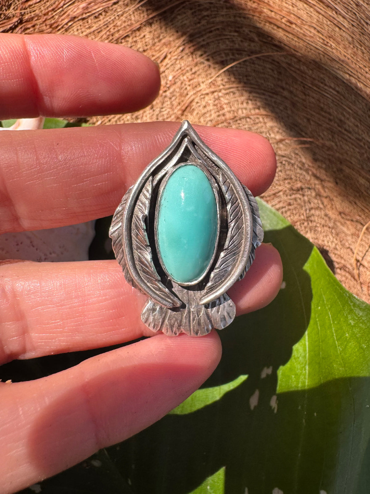 Silver ring in styllized bird shapwith a blue turquoise stone held between fingers against a natural background 