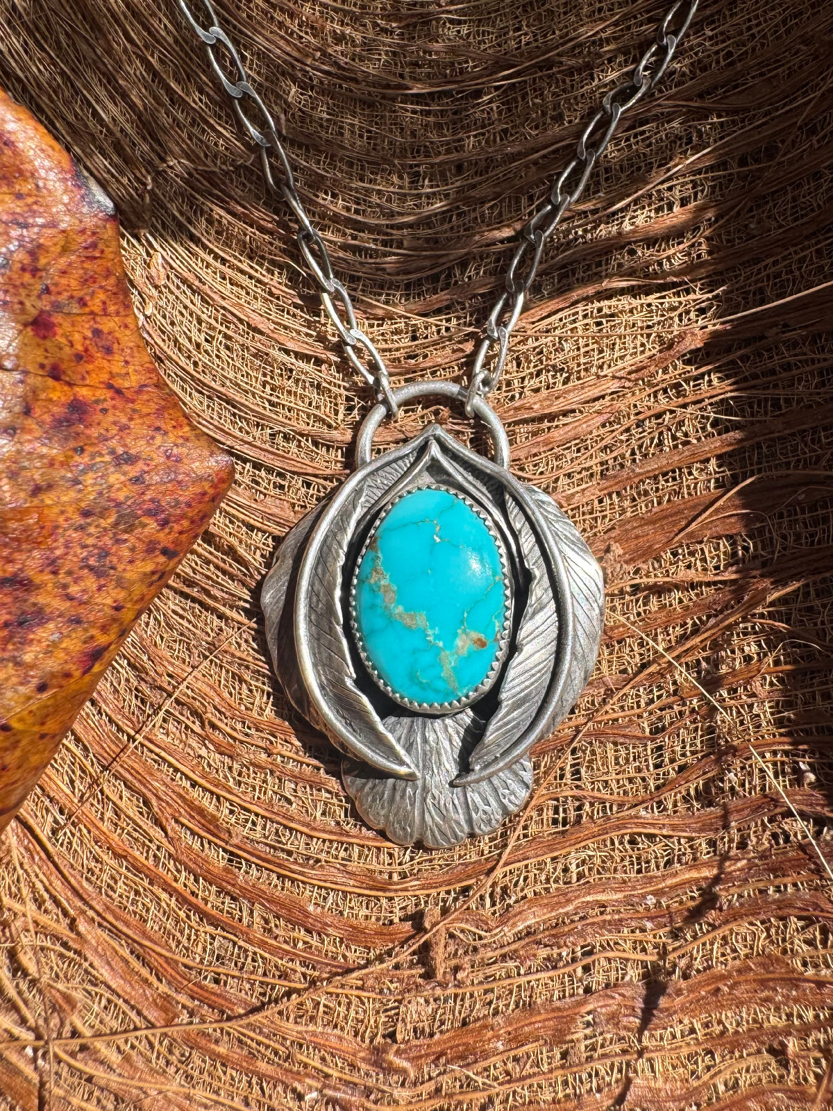 Silver stylized bird necklace with blue turquoise pendant on a wooden surface