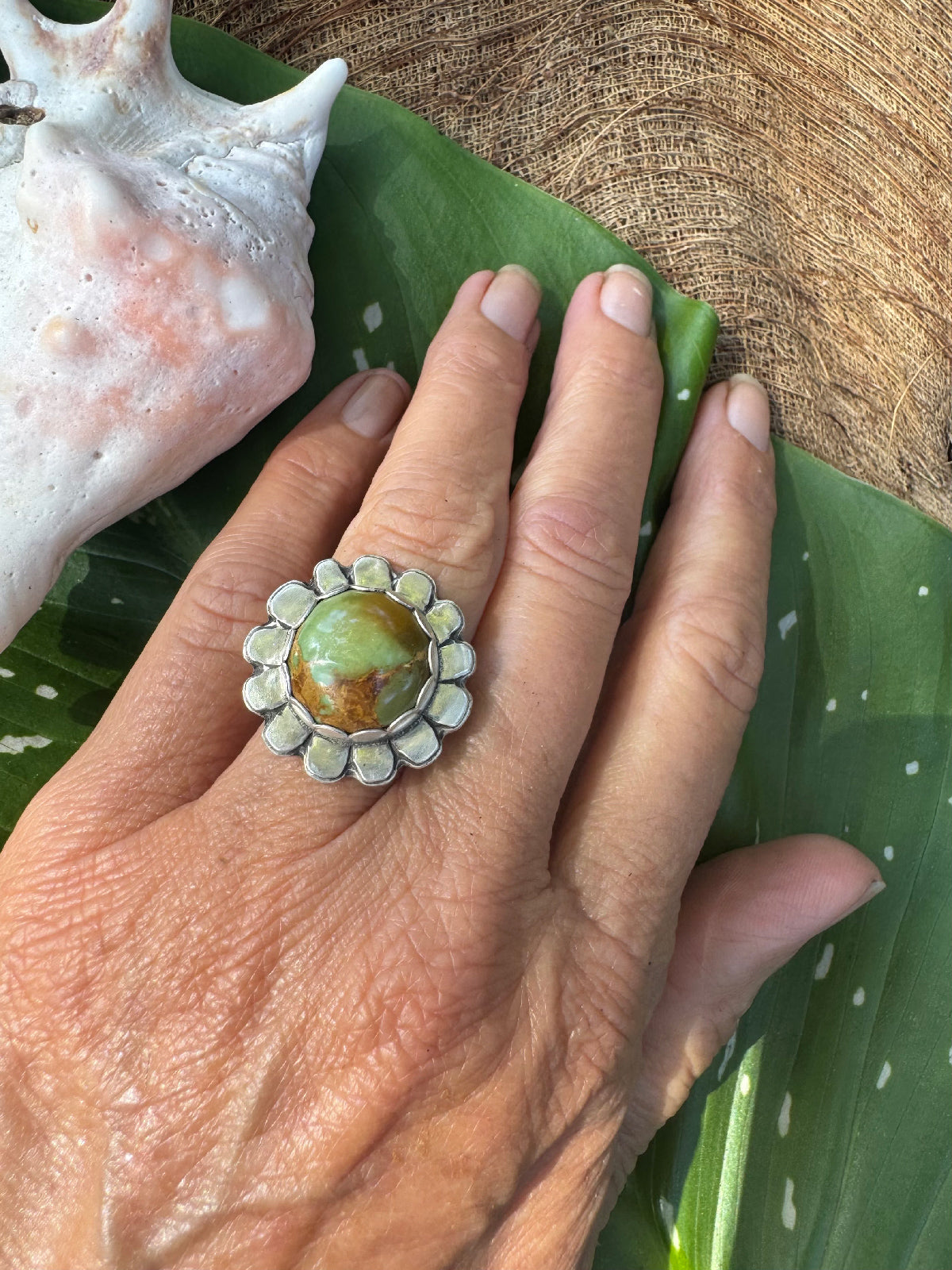 Hand wearing a silver flower ring with a green stone on a leafy background