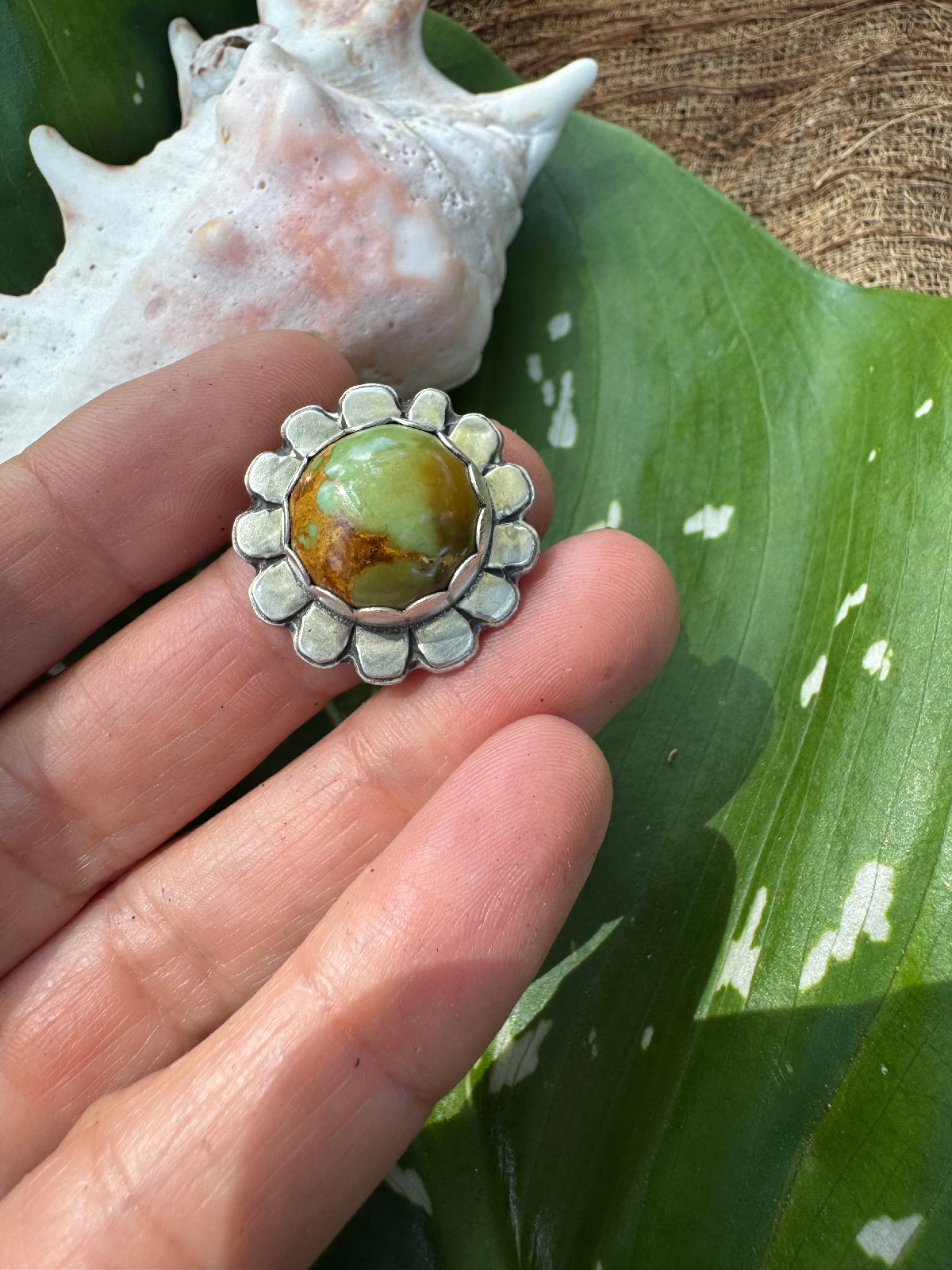 Silver ring with a green gemstone held between fingers against a natural background