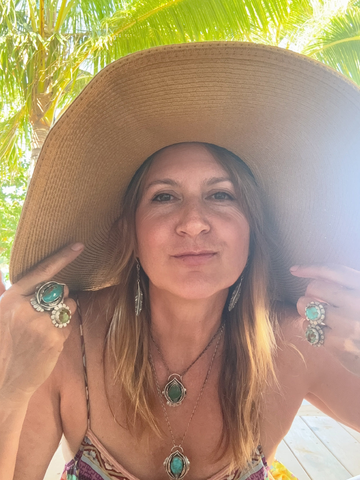 Woman wearing a wide-brimmed hat and multiple turquoise rings and neckalces palm tree in the background