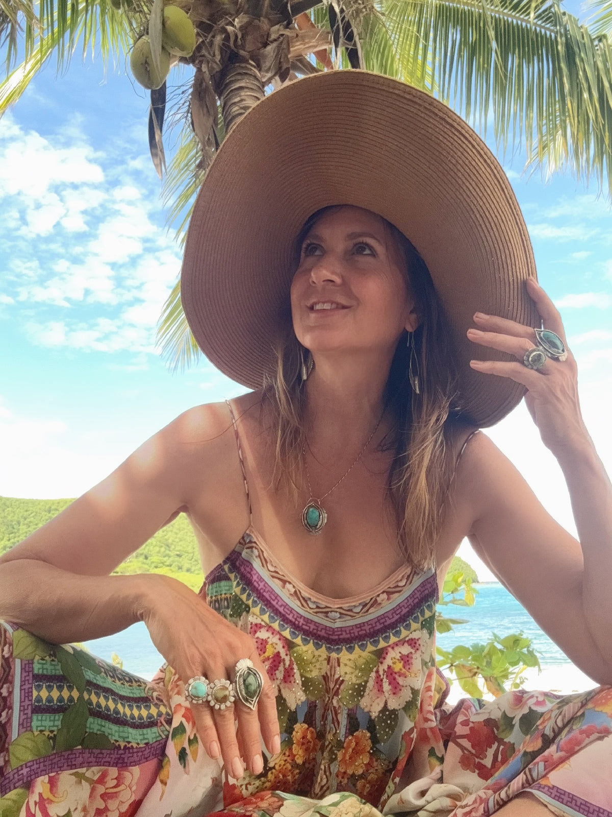 Woman wearing a large sun hat, turquoise jewelry and colorful dress with a tropical background