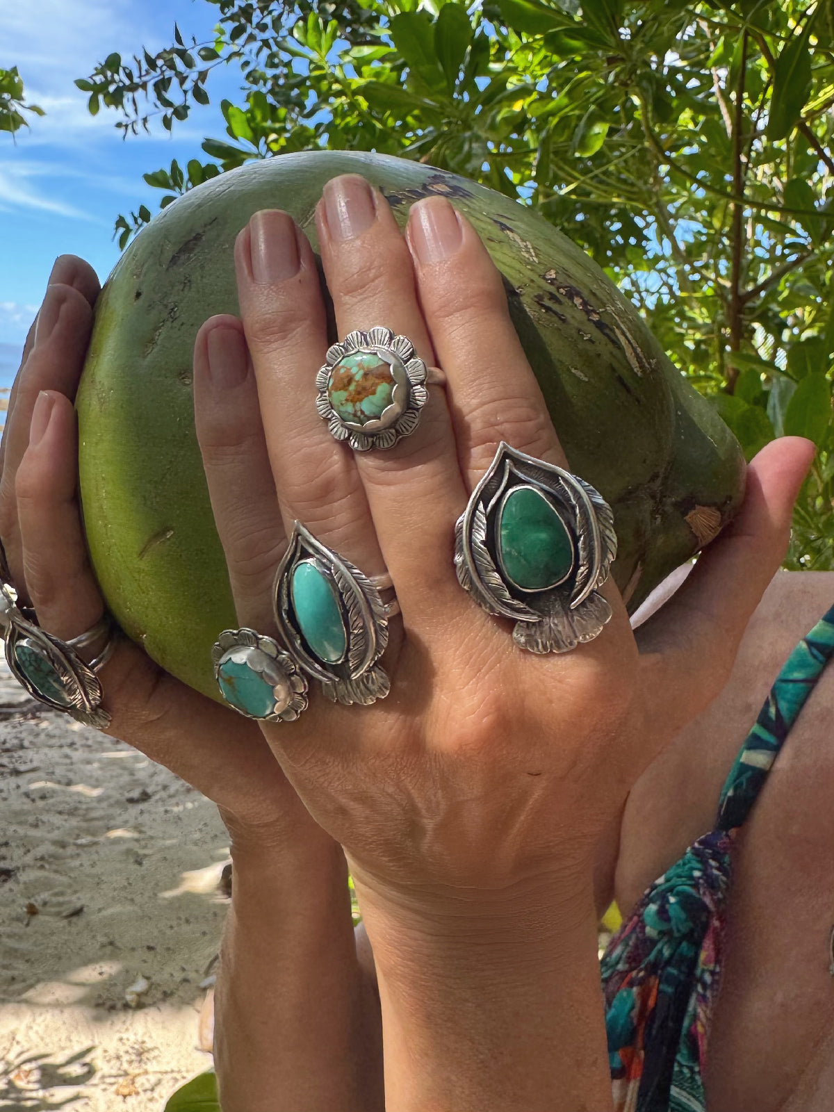 Hands wearing silver rings with turquoise stones against a natural background