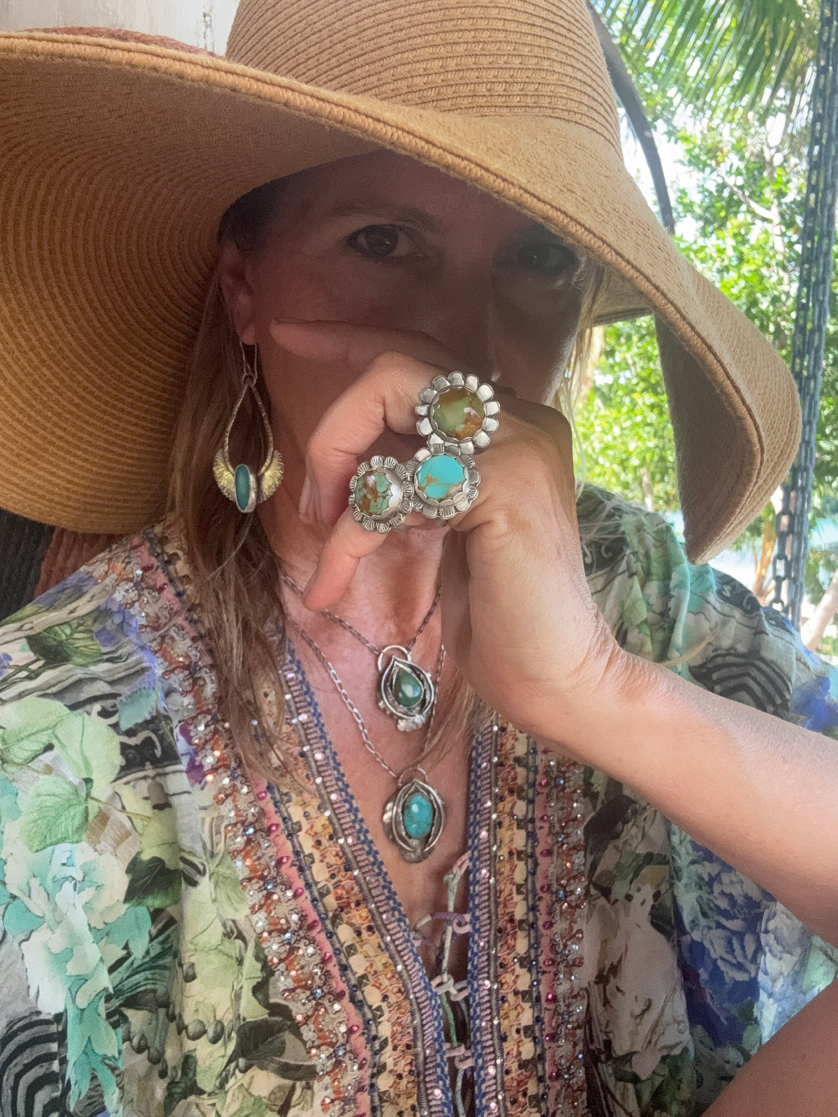 Person wearing a wide-brimmed hat and colorful flower rings outdoors